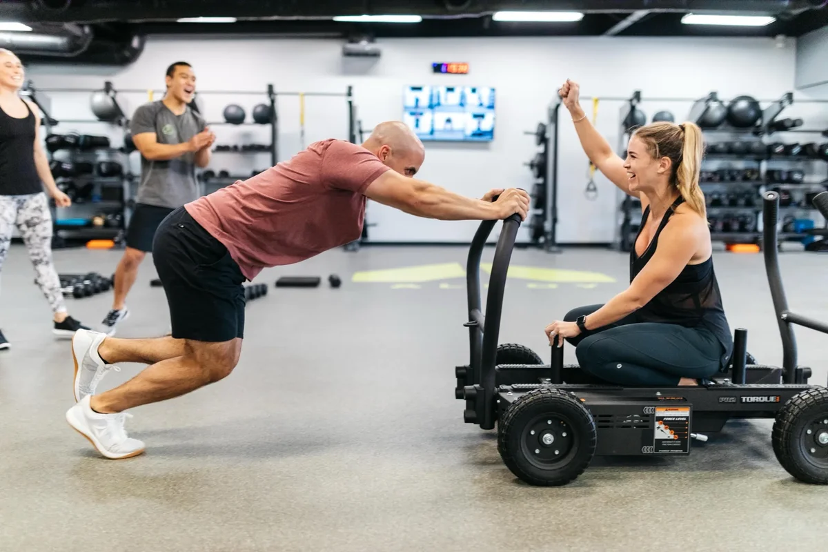 Members share a laugh around the sled between sets at an Alloy Personal Training studio