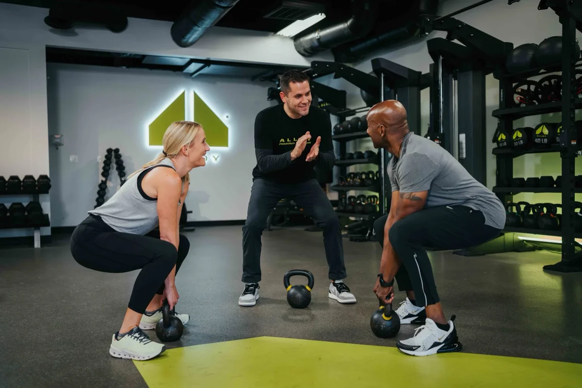 A coach talks with members between exercises during a small group session at an Alloy Personal Training studio