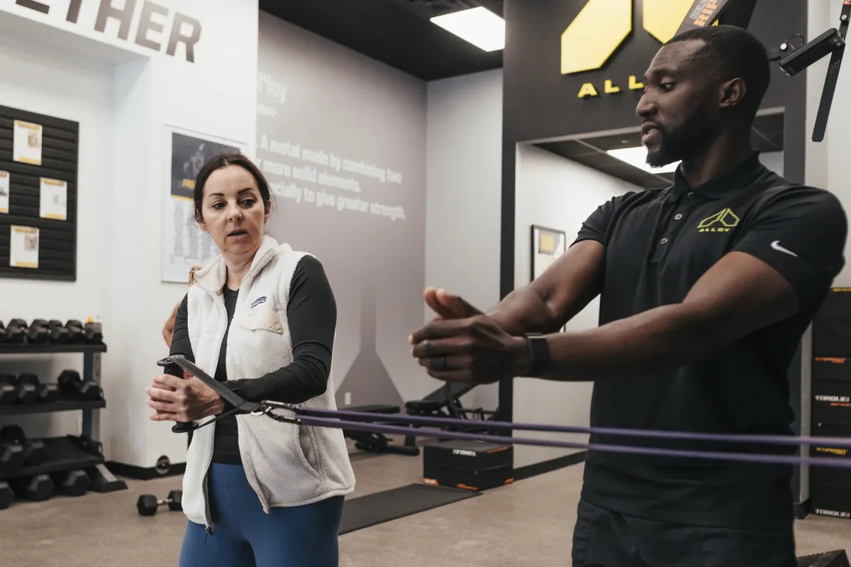 A coach demonstrates a resistance band movement for a member at Alloy Personal Training Ahwatukee Foothills