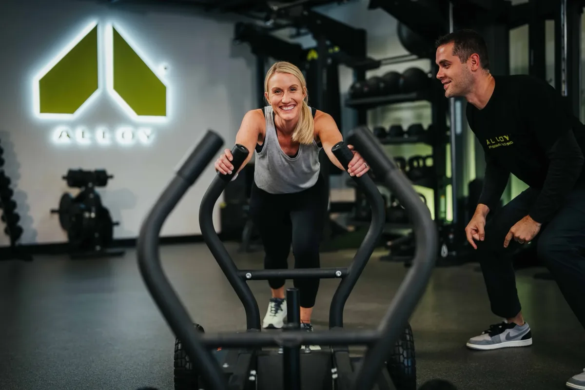 A coach cheers on a member pushing a weighted training sled during a small group session